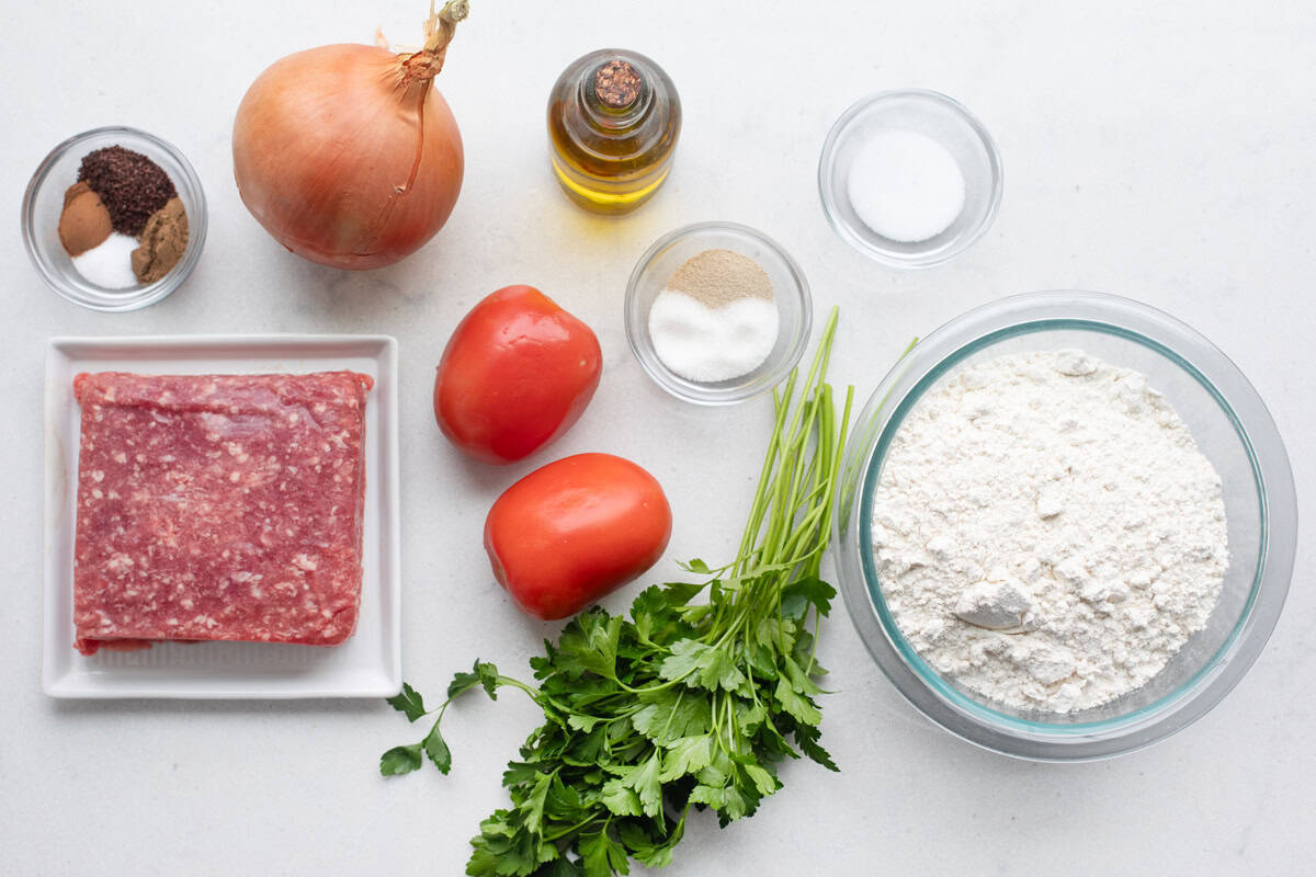 Ingredients for bakery style meat pie recipe: ground beef, spices, onions, tomato, oil, flour.