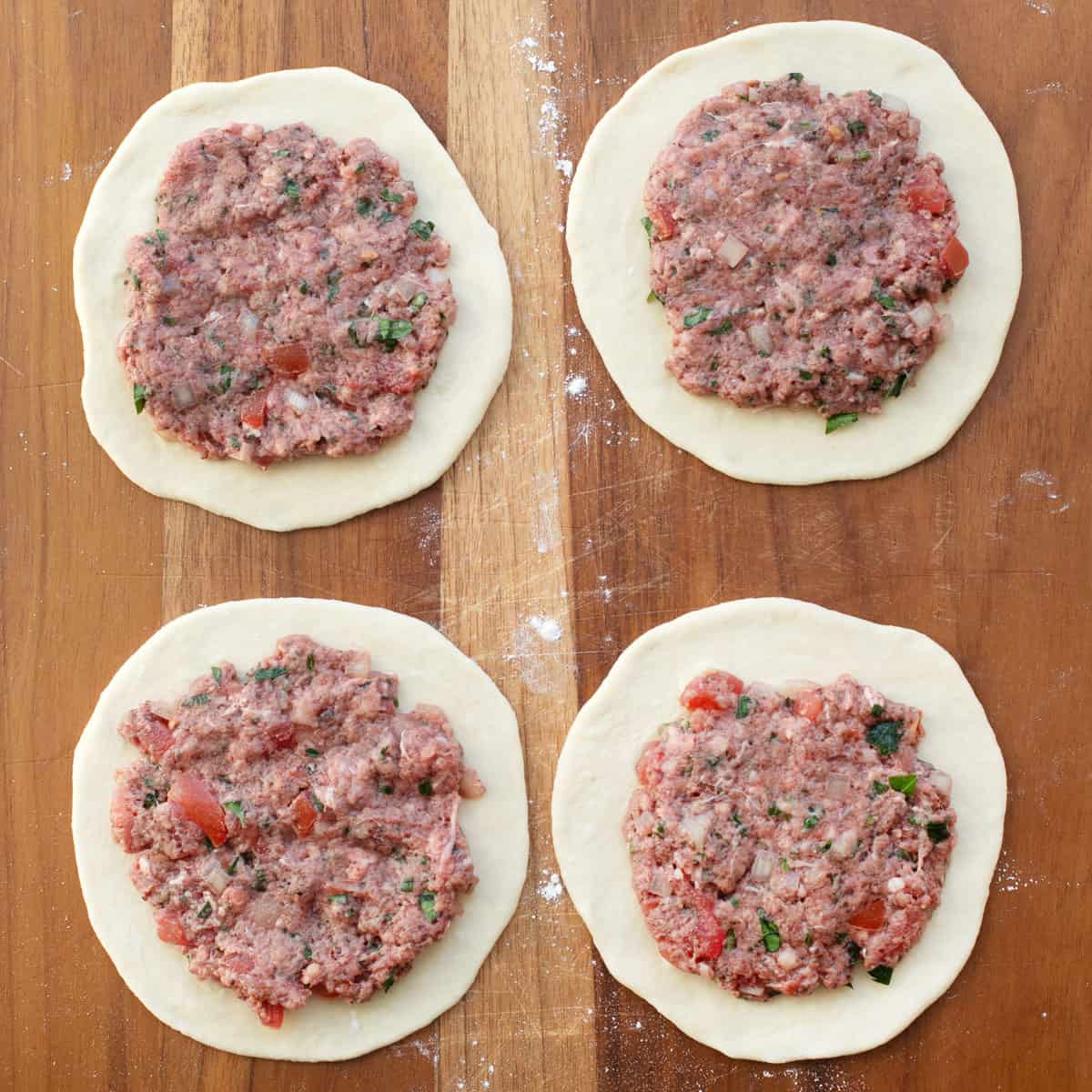 Spiced beef filling smashed on top of flat round dough pieces before shaping.