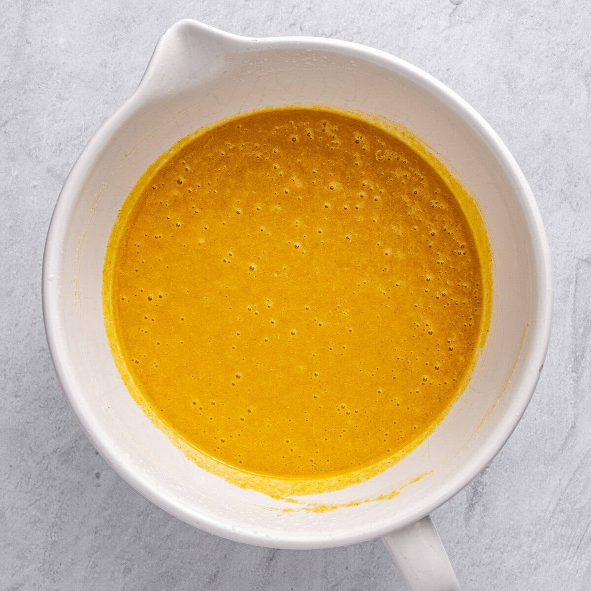 Bright orange cake batter in a mixing bowl after combining wet and dry ingredients.