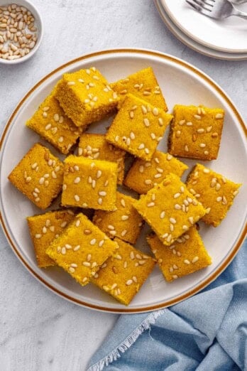 Easy Lebanese turmeric cake called stouf cut into squares with pine nuts baked o top.
