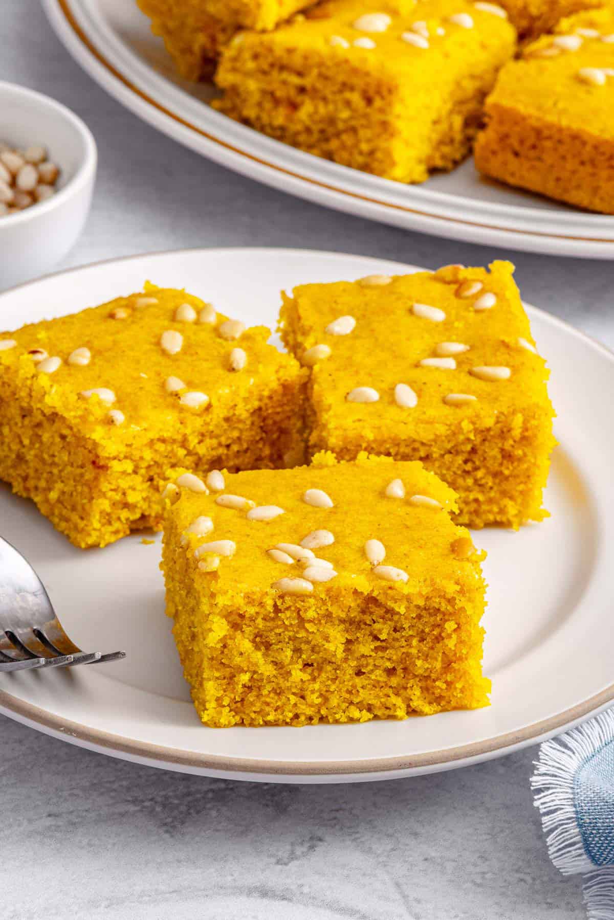 Soft sfouf turmeric cake squares on a small plate with pine nuts baked on top.