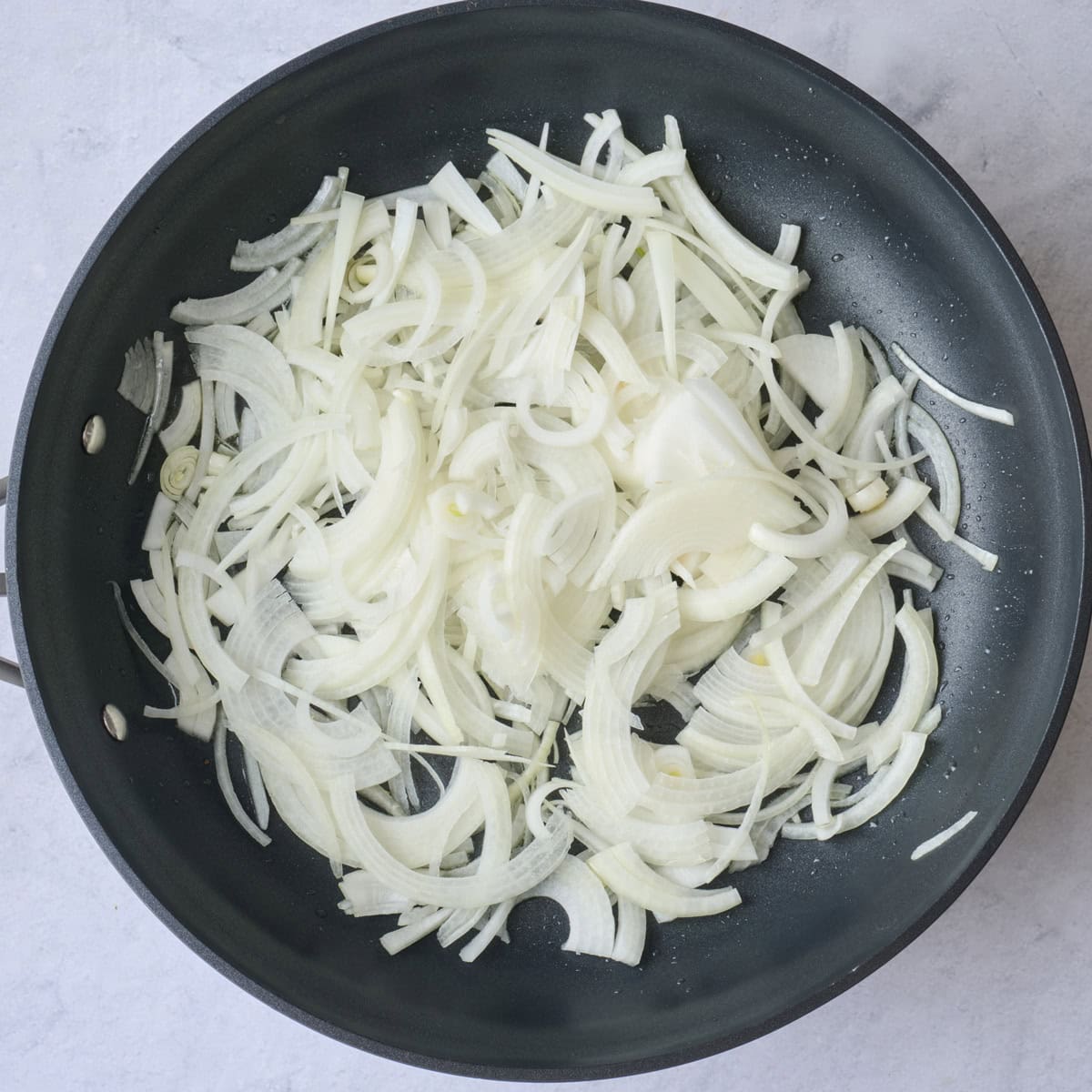 Sliced onions in a skillet before cooking.