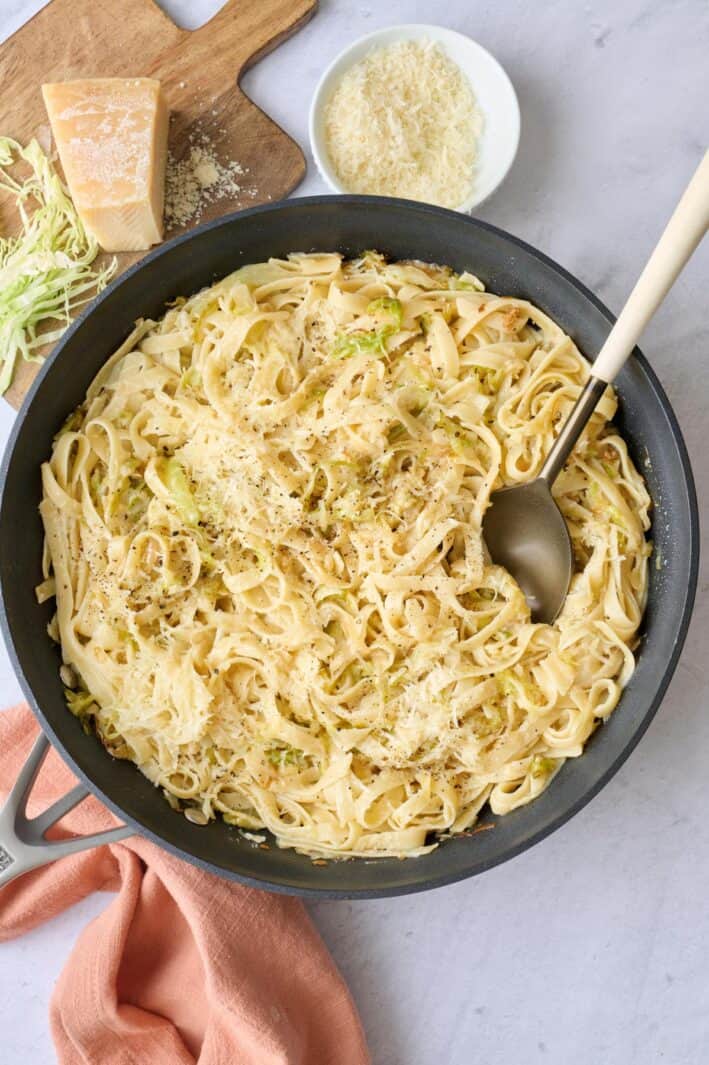 Cabbage pasta in the skillet garnished with black pepper and extra parmesan with serving fork dipped inside.