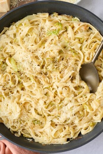 Cabbage pasta in the skillet garnished with black pepper and extra parmesan with serving fork dipped inside.
