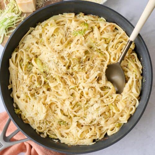 Cabbage pasta in the skillet garnished with black pepper and extra parmesan with serving fork dipped inside.