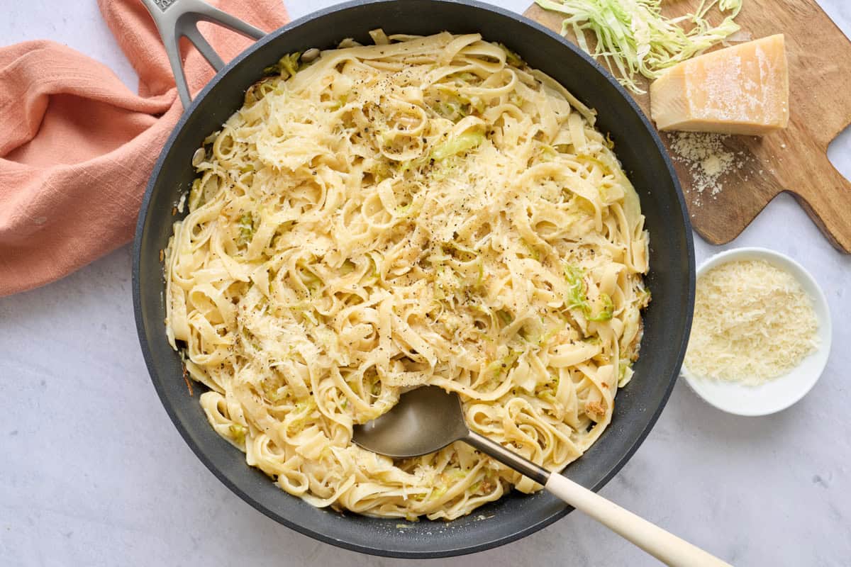 Cabbage pasta in the skillet garnished with black pepper and extra parmesan with serving fork  dipped inside.