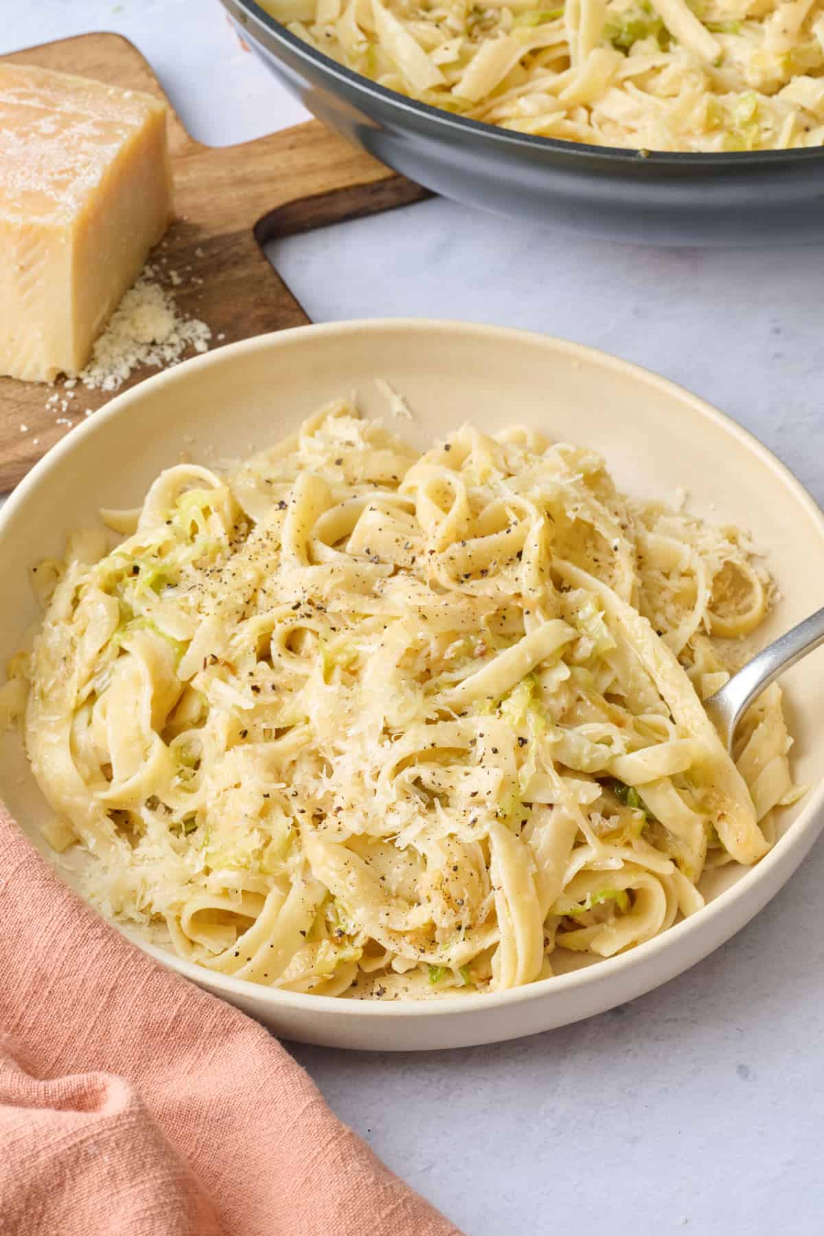 Avocado pasta salad in a serving bowl with serving set dipped inside or nearby, halved avocado nearby.