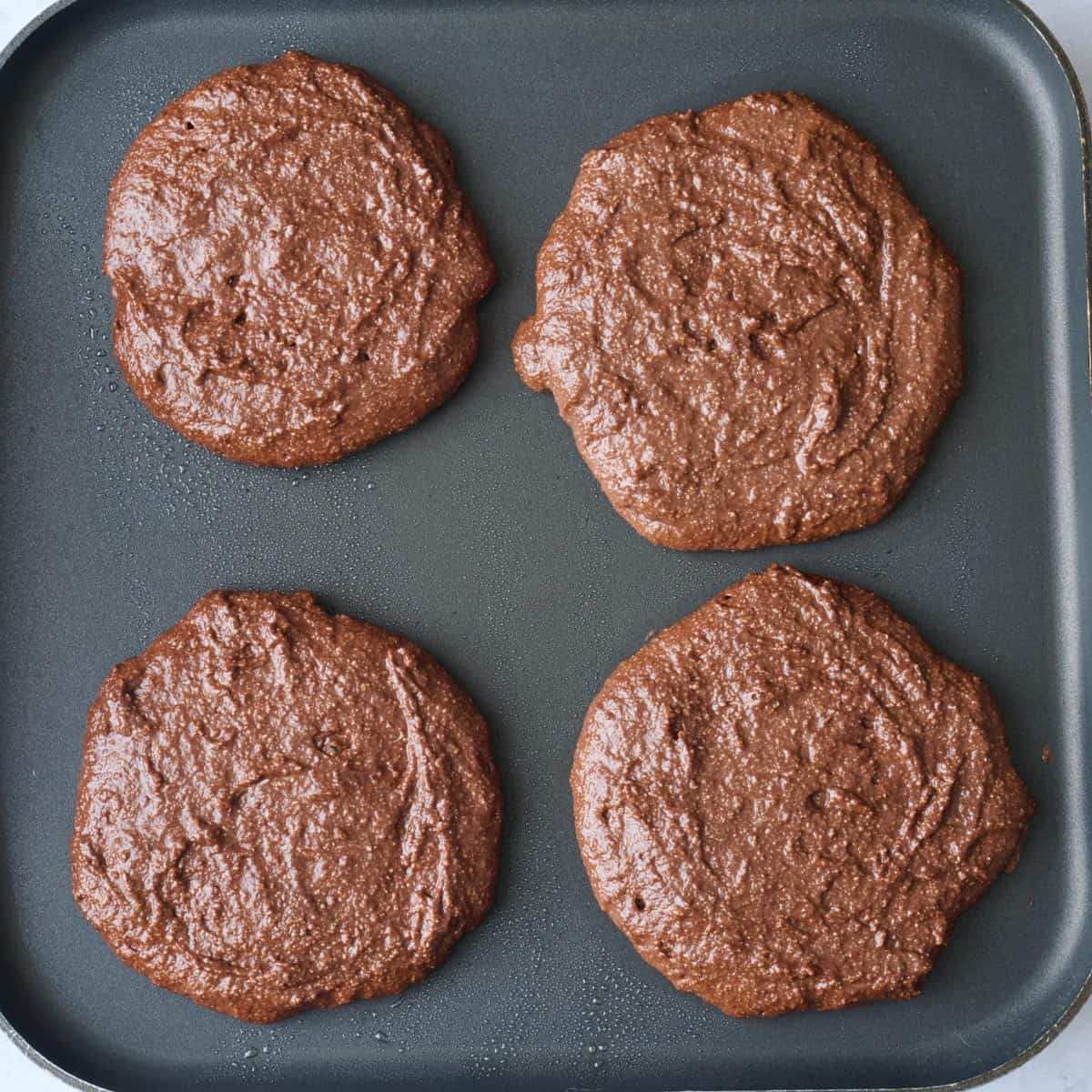 4 thick chocolate protein pancakes on a hot griddle before cooking.