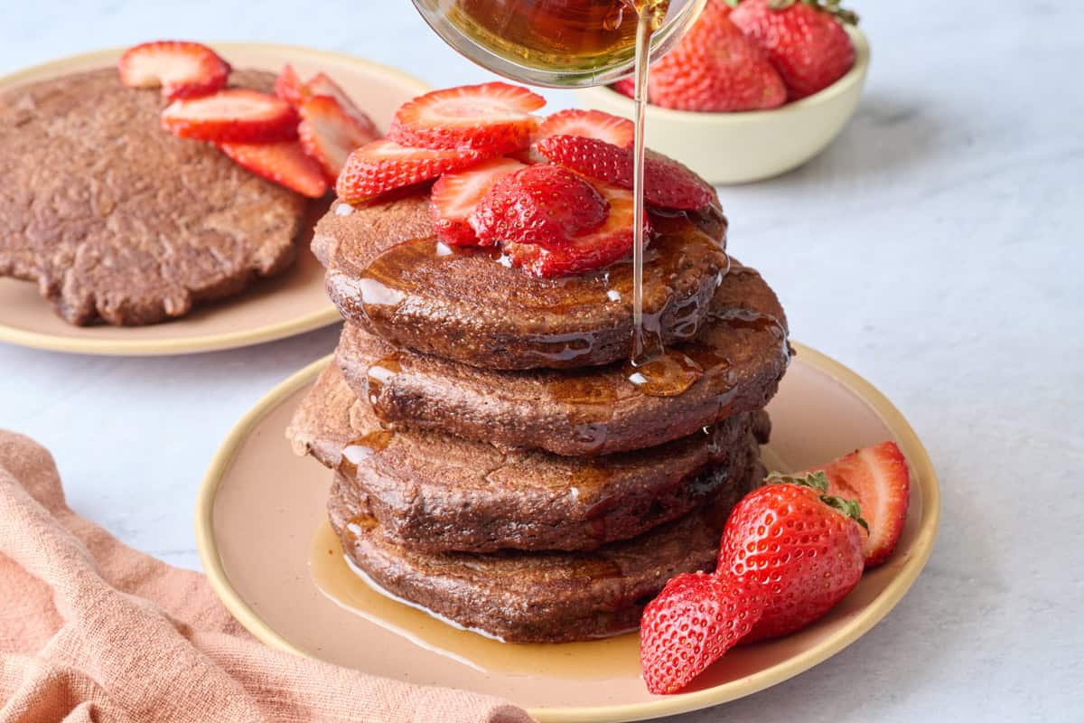 High protein chocolate pancakes recipe stacked on a plate with strawberries and maple syrup.