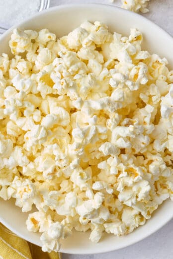 Popcorn in a bowl with the paper bag, laying down with some pouring out onto the surface, small dish of salt nearby.