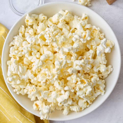 Popcorn in a bowl with the paper bag, laying down with some pouring out onto the surface, small dish of salt nearby.