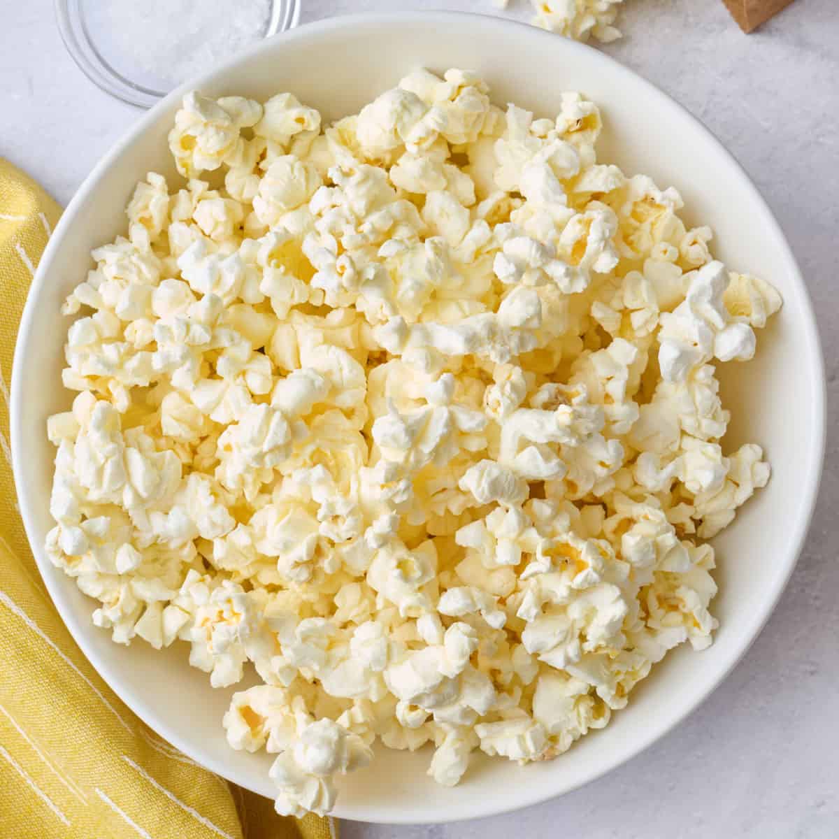 Popcorn in a bowl with the paper bag, laying down with some pouring out onto the surface, small dish of salt nearby.
