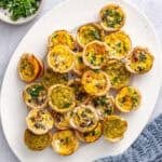 Mini quiches on a platter garnished with chopped parsley.