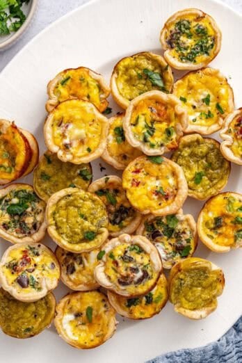 Mini quiches on a platter garnished with chopped parsley.