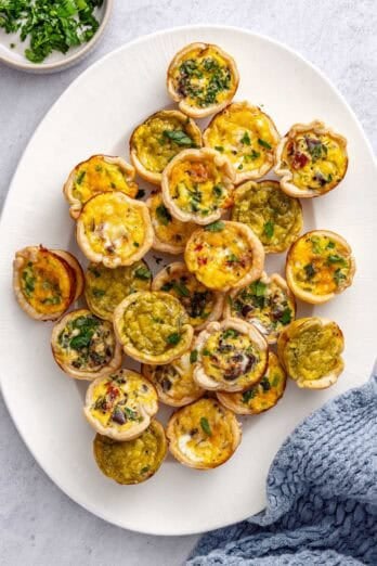 Mini quiches on a platter garnished with chopped parsley.
