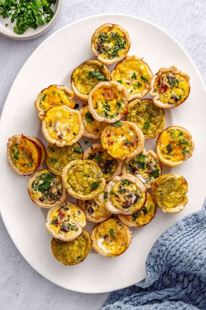 Mini quiches on a platter garnished with chopped parsley.