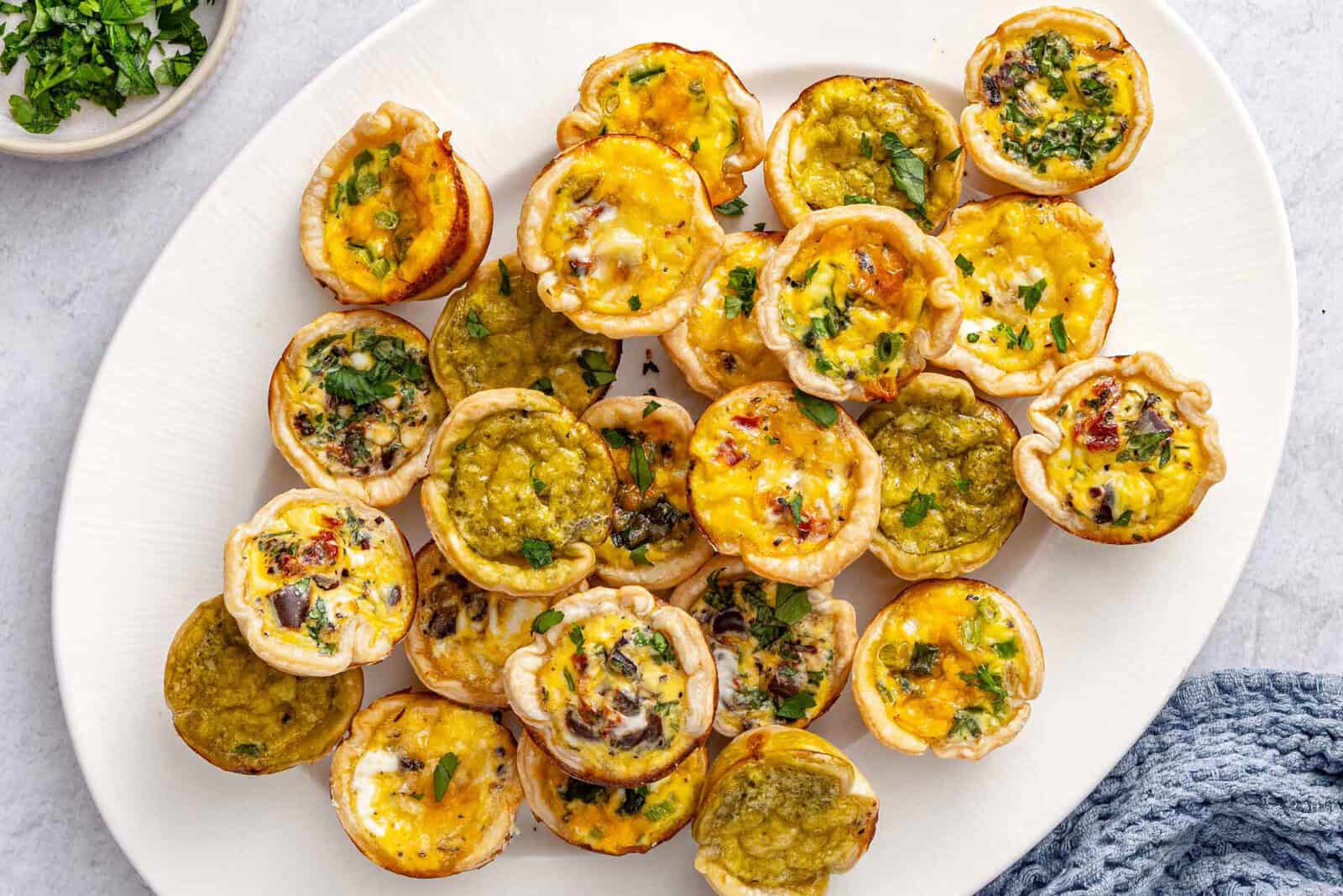 Mini quiches on a platter garnished with chopped parsley.