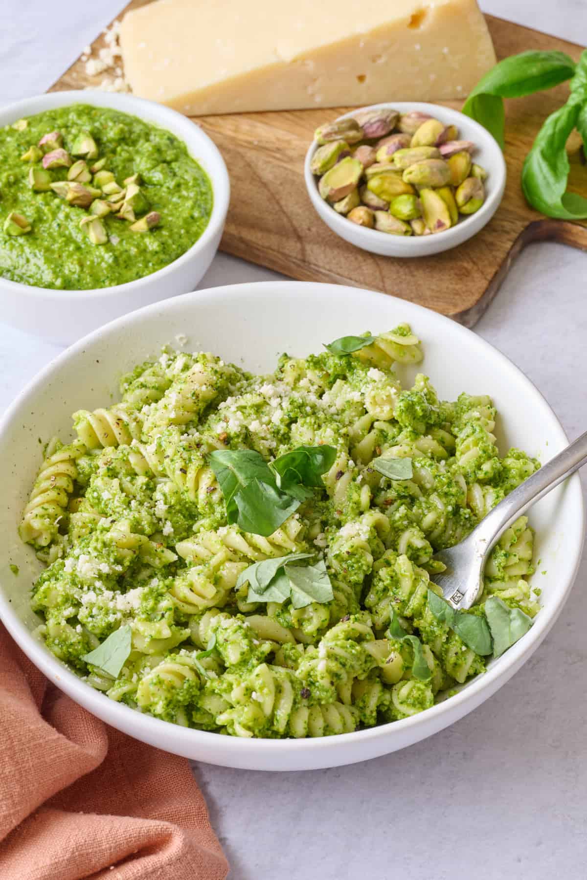 Pistachio pesto tossed with pasta in a small shallow bowl, with a small jar of pesto nearby.