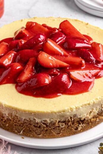 Whole strawberry cheesecake on a round platter with a small dish of extra strawberry sauce nearby.