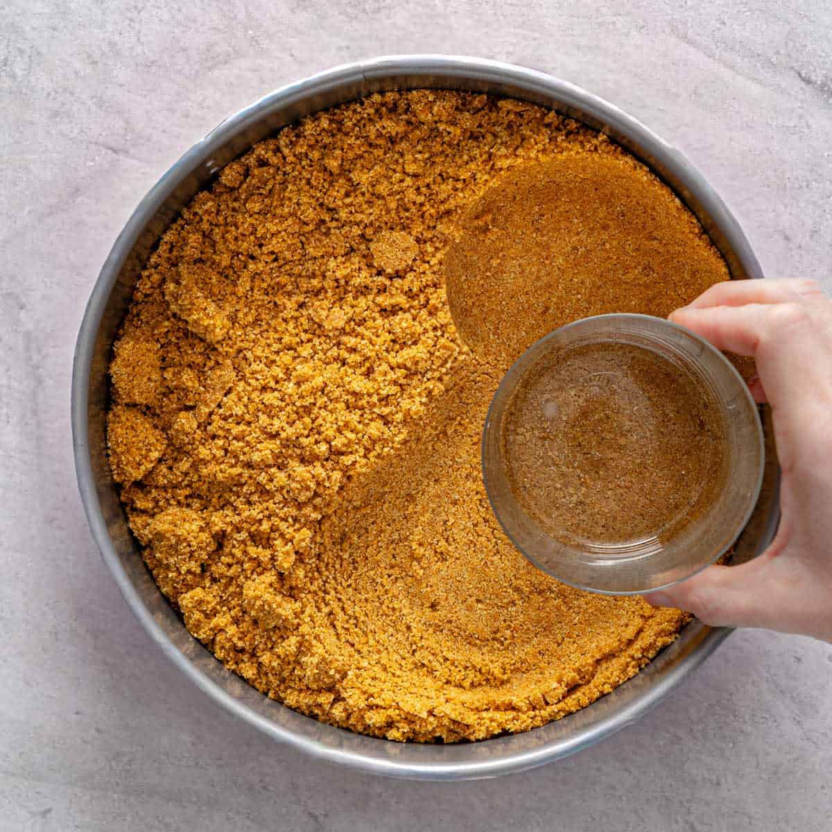 Crumbs being pressed into a springform pan with a glass cup.