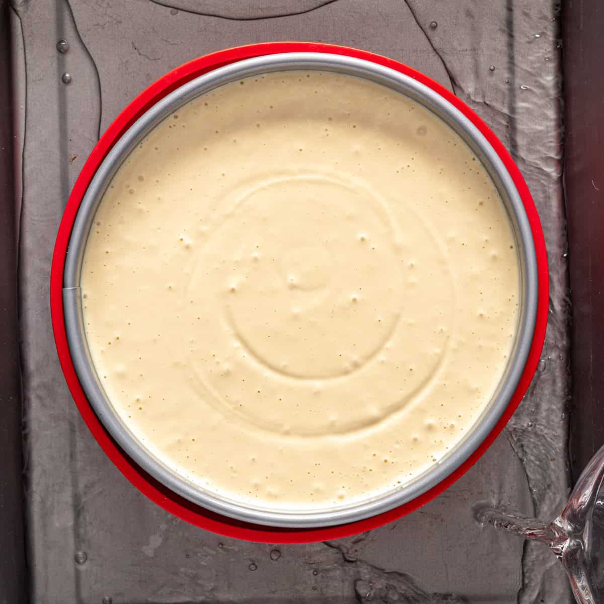 Cheesecake pan in a large roasting pan with water being poured in.
