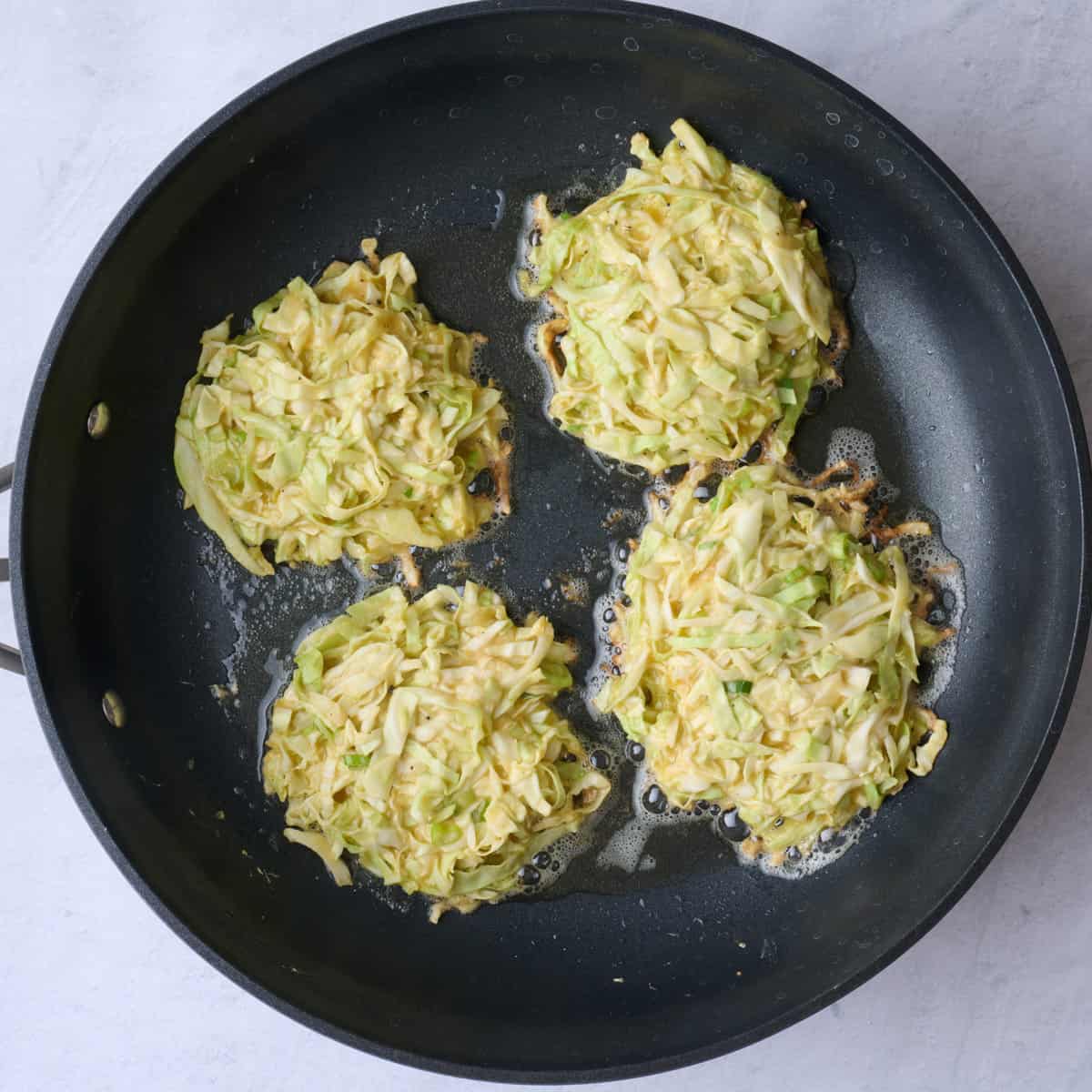 4 scoops of mixture on a large non-stick oiled skillet after flattening into round pancakes.