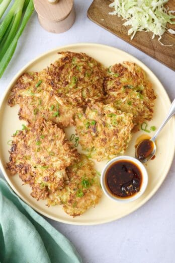 Cabbage pancakes on a platter garnished with extra sliced green onions and with a small dish of chili crisp.