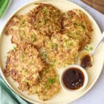 Cabbage pancakes on a platter garnished with extra sliced green onions and with a small dish of chili crisp.