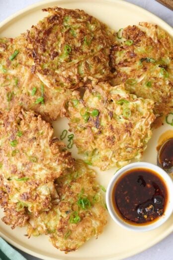 Cabbage pancakes on a platter garnished with extra sliced green onions and with a small dish of chili crisp.