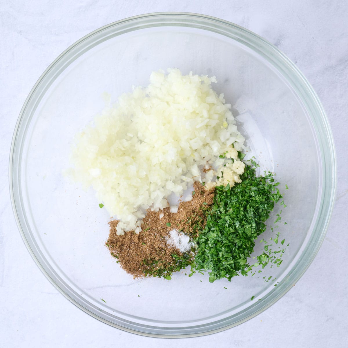 Onion, garlic, parsley, spices, salt, and pepper in a bowl.