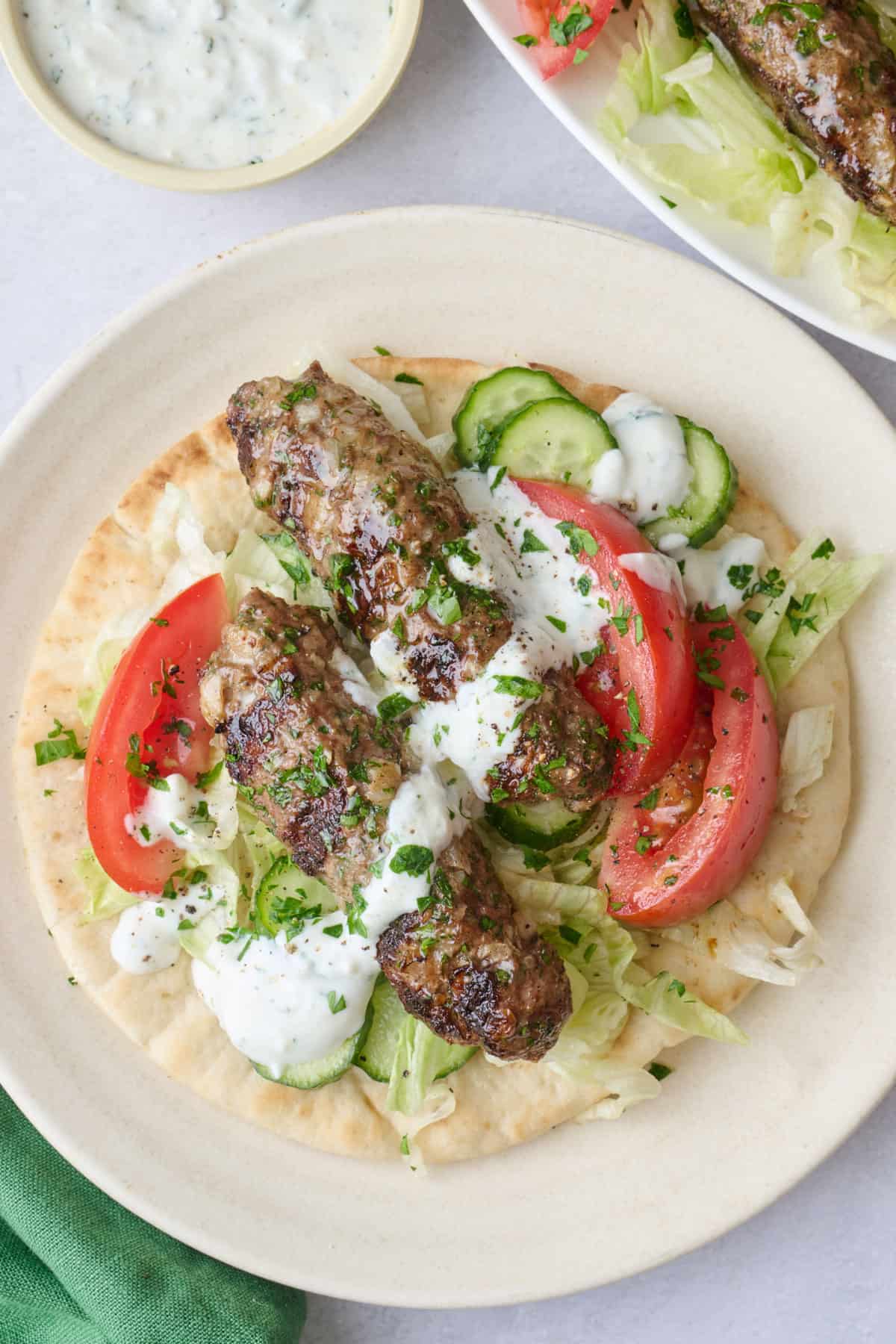 2 lamb kabobs served on top of open faced pita with cucumber, wedge tomatoes, lettuce on top, drizzled with yogurt sauce.