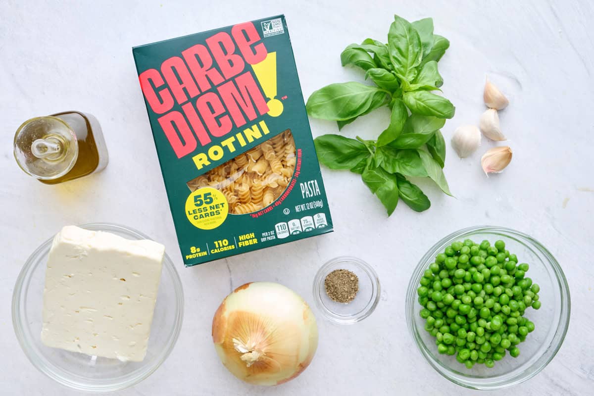 Ingredients for pasta recipe: oil, Carbe Diem Rotini, feta block, onion, fresh basil, peas, pepper, and garlic cloves.