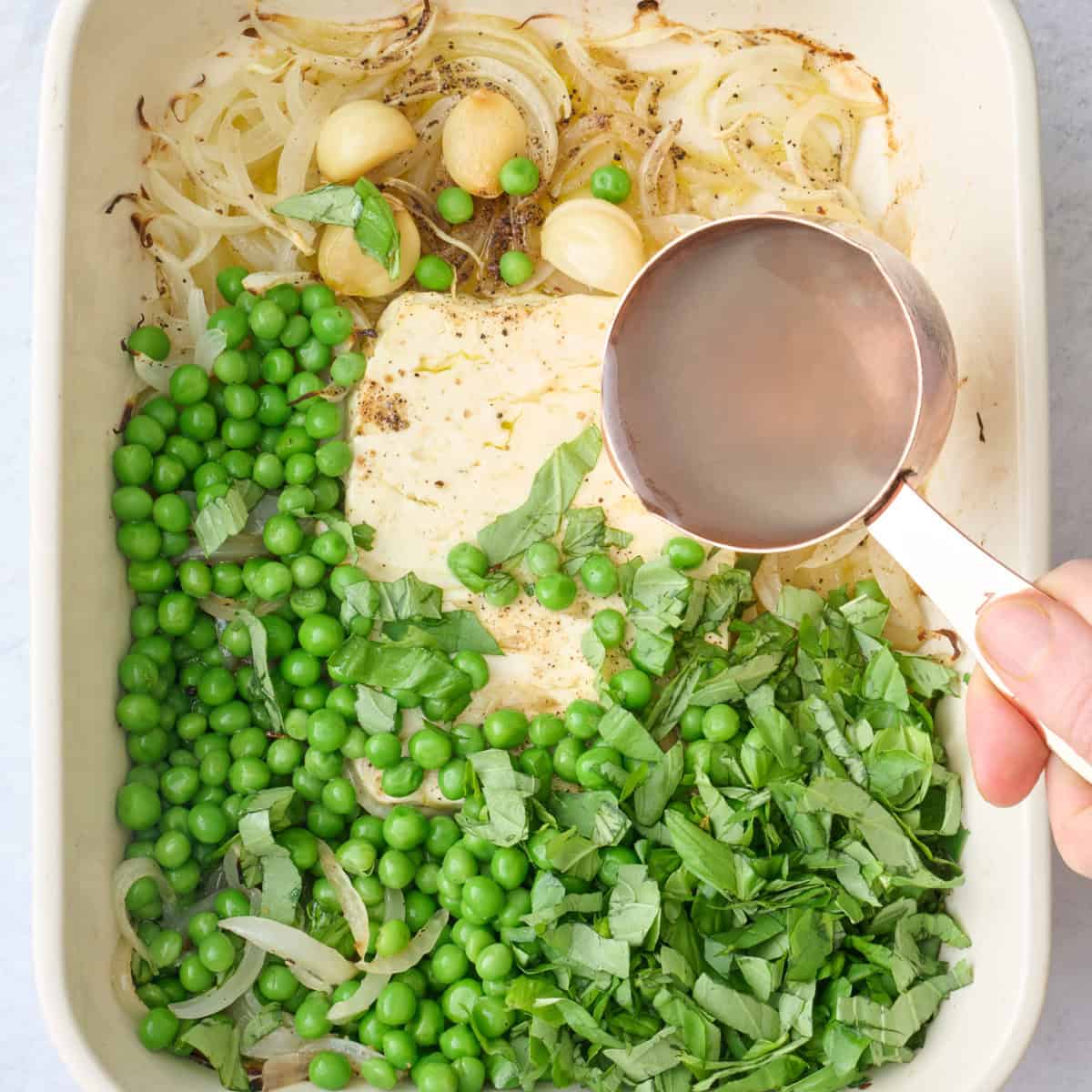 Pasta water being added to baking dish with baked feta and green sauce ingredients.