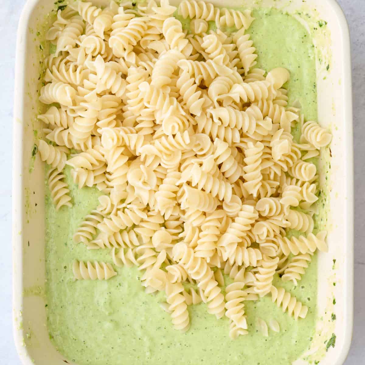 Cooked pasta added on top of creamy green feta pasta sauce in a baking dish before tossing.