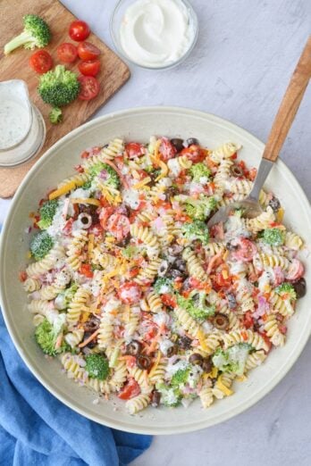 Ranch pasta salad in a serving bowl with serving spoon dipped inside, small dish of extra fresh herbs nearby.
