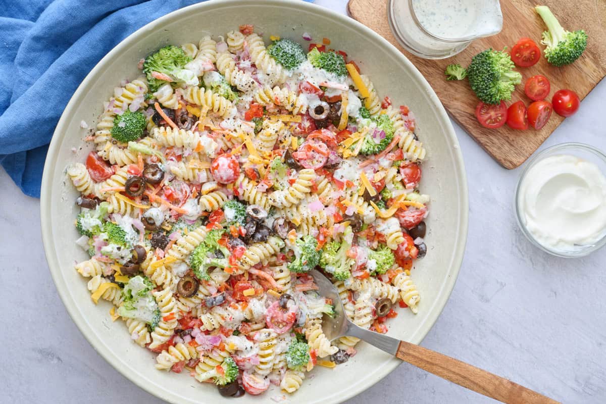Ranch pasta salad in a serving bowl with serving spoon dipped inside, small dish of extra fresh herbs nearby.