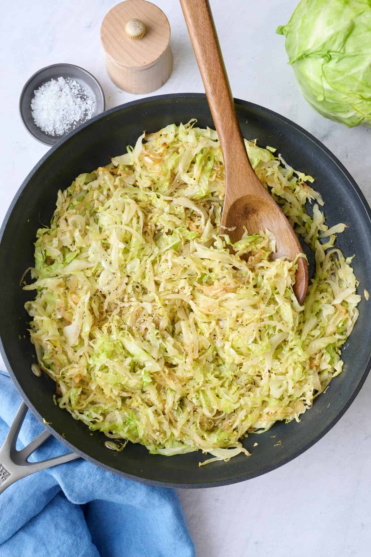 Sauteed cabbage in skillet with serving set, salt and pepper nearby.