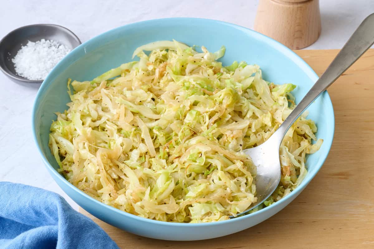 Sauteed cabbage in a shallow bowl with serving set dipped into side.
