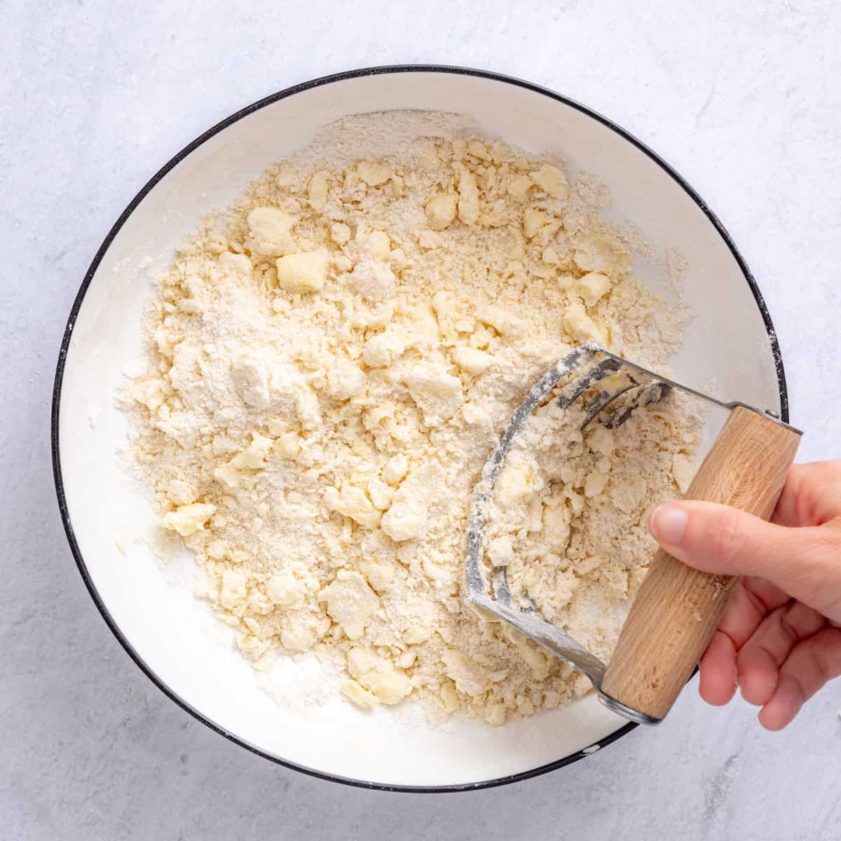 Hands or pastry cutter cutting the butter into the flour mixture.