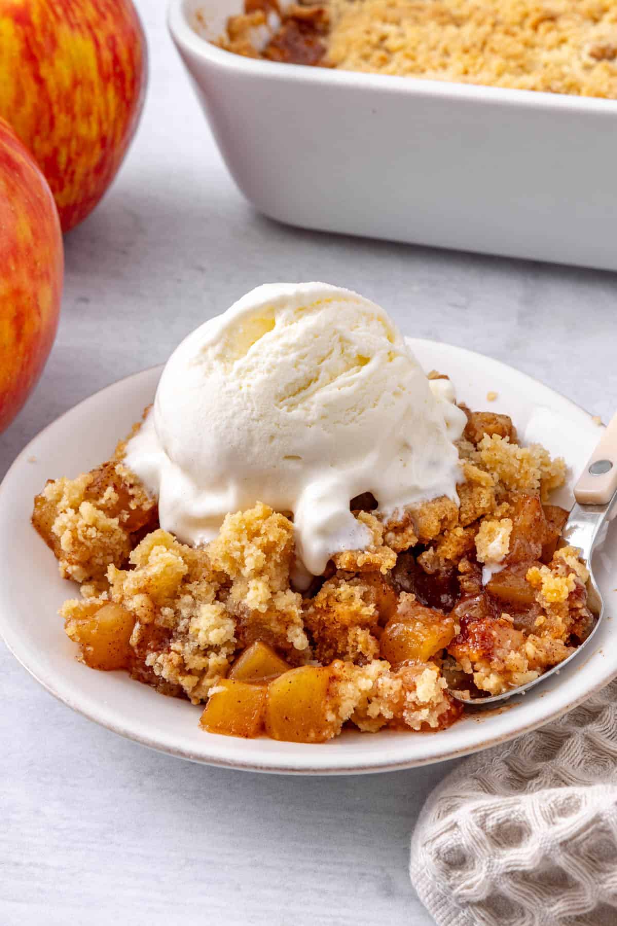 Serving of apple crumble in a small shallow bowl with ice cream served on top.