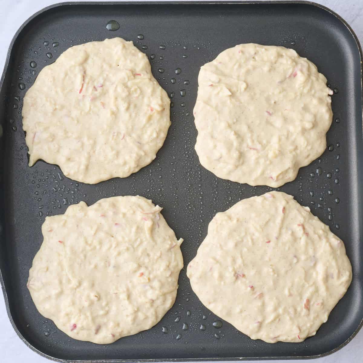 4 pancakes on a griddle before cooking.