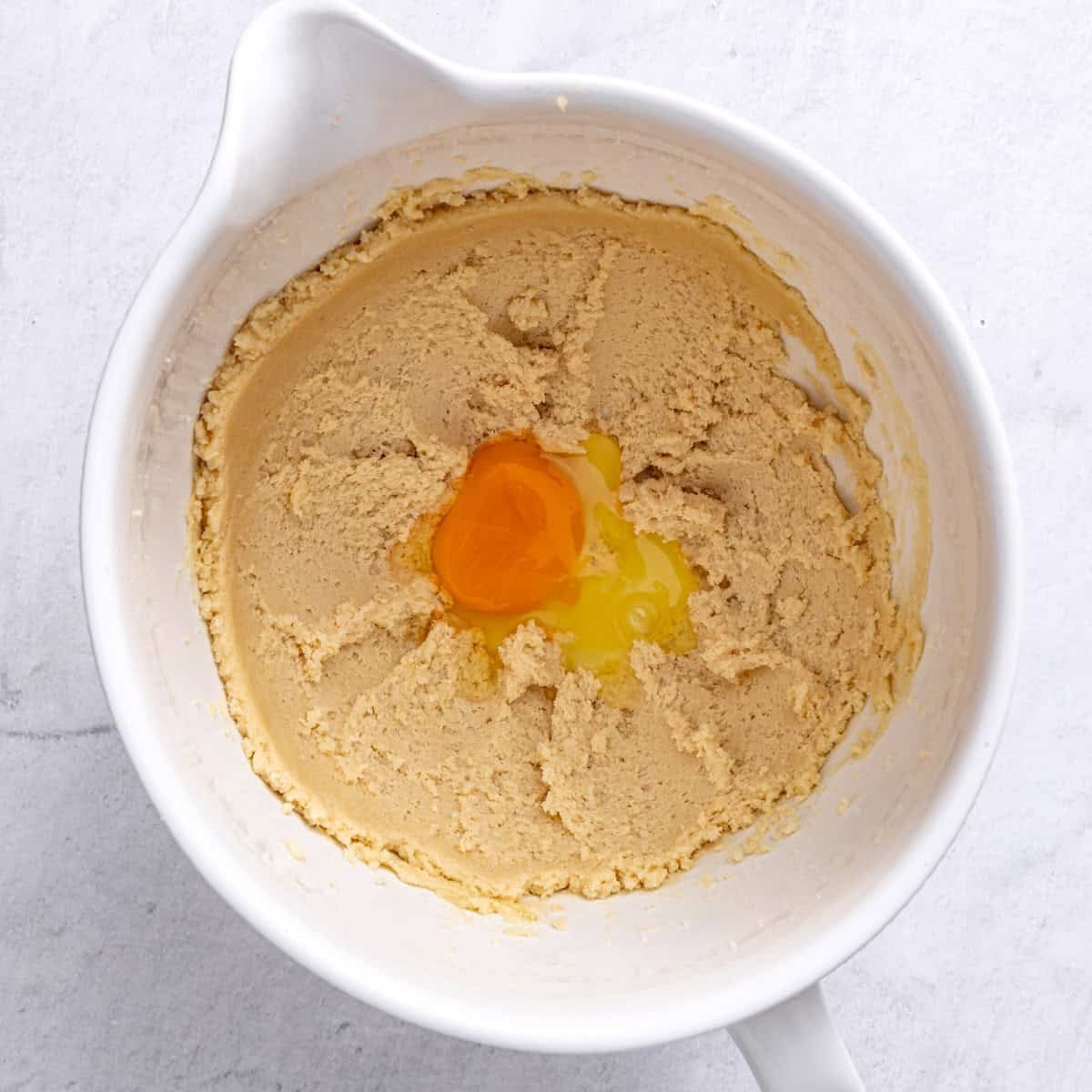 A bowl consisting of butter and sugar after creaming with 1 egg added.
