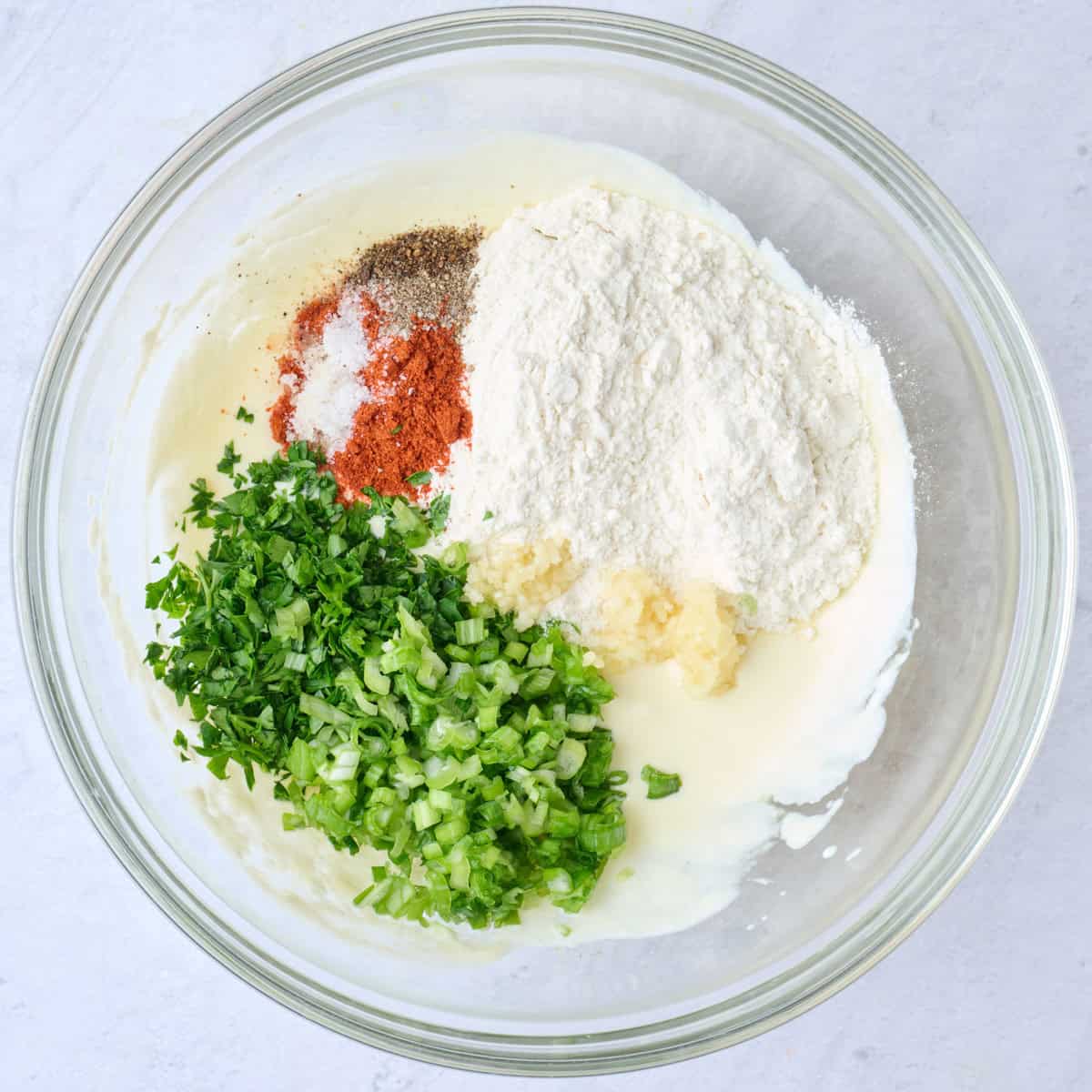 Yogurt and egg after whisked in a bowl with flour, garlic, green onions, parsley, salt, pepper and paprika added.