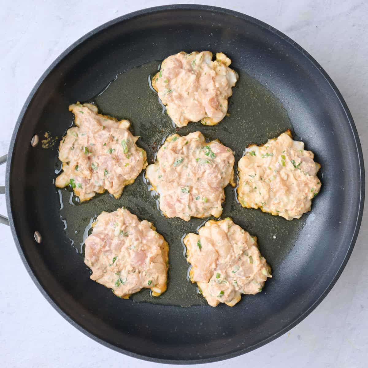 5 fritters scooped into an oiled pan before cooking.