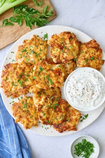 Chicken fritters on a platter garnished with chopped parsley, served with yogurt sauce.