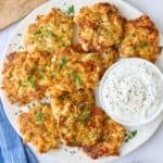 Chicken fritters on a platter garnished with chopped parsley, served with yogurt sauce.