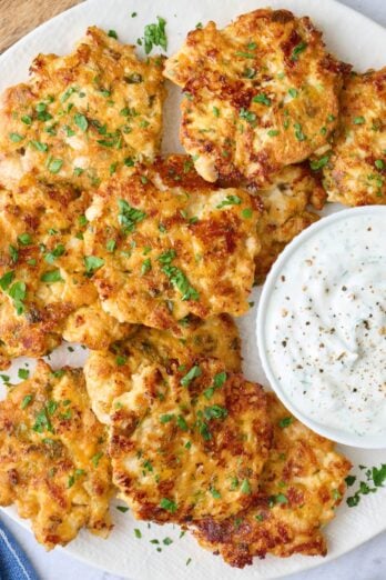 Chicken fritters on a platter garnished with chopped parsley, served with yogurt sauce.