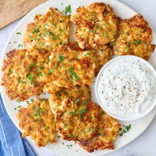 Chicken fritters on a platter garnished with chopped parsley, served with yogurt sauce.