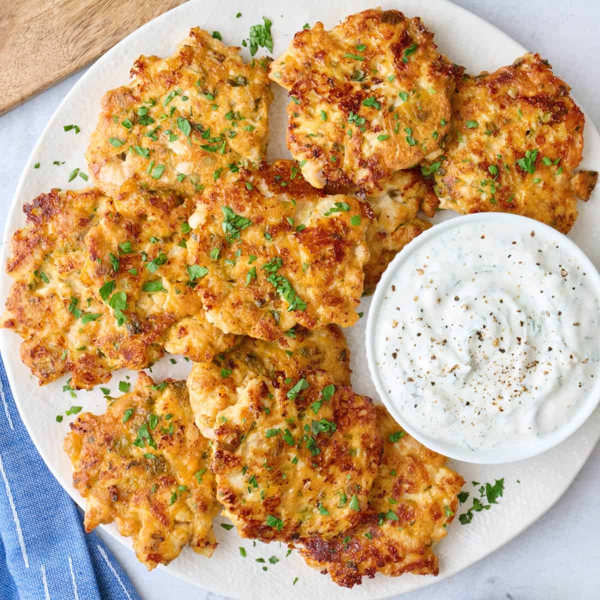 Chicken fritters on a platter garnished with chopped parsley, served with yogurt sauce.
