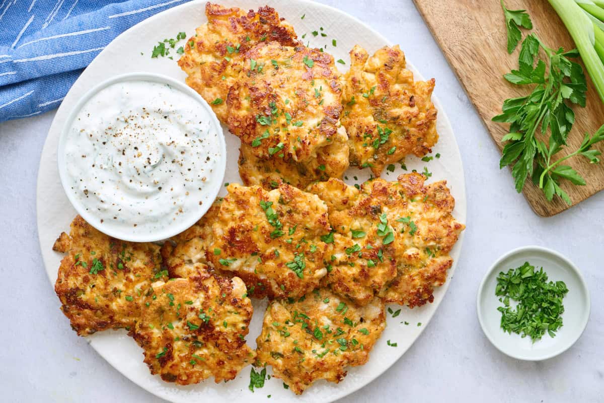 Chicken fritters on a platter garnished with chopped parsley, served with yogurt sauce.